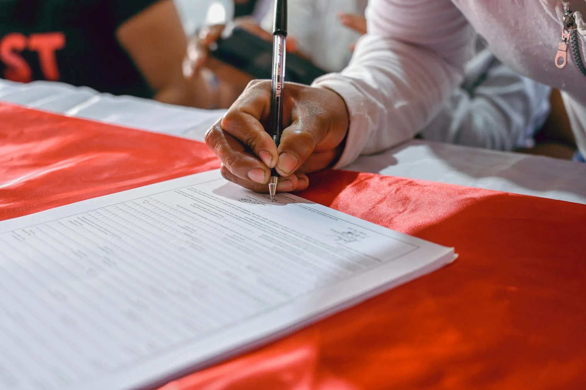 Hand signing a form on a red tablecloth
