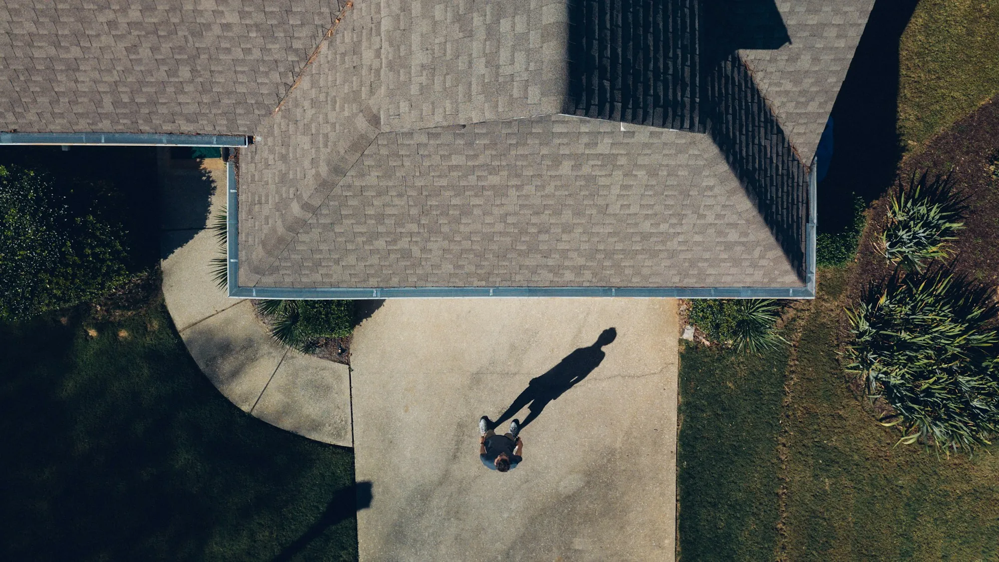 Aerial view of a shingle roof corner and a person's shadow on the walkway below