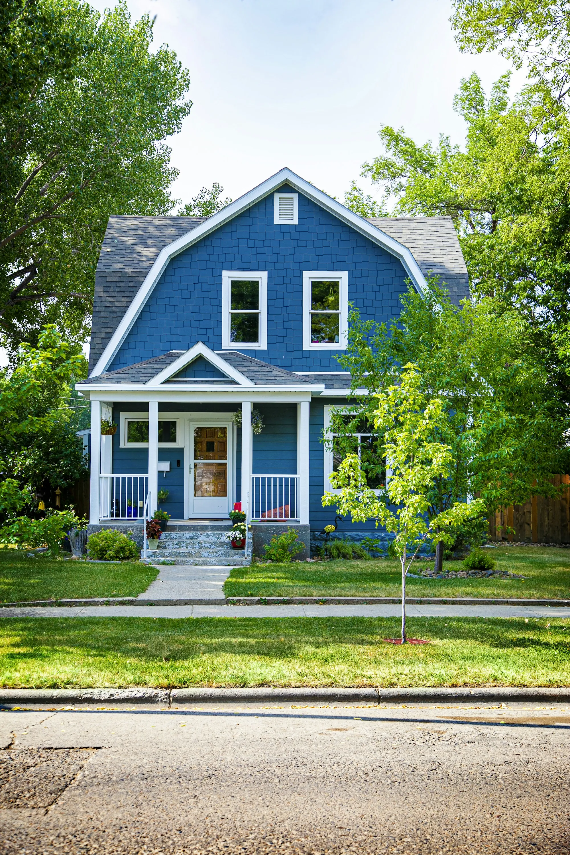 Blue house with a white front porch and a young tree in the yard